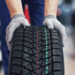 Closeup of mechanic hands pushing a black tire in the workshop.